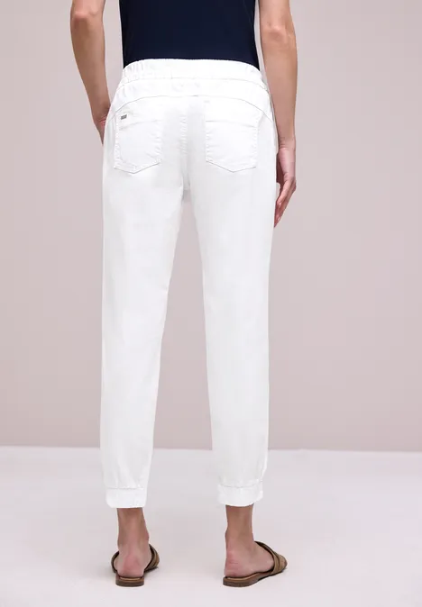 Rückenansicht einer Person in weißen Hosen, die lässig in braunen Sandalen steht.