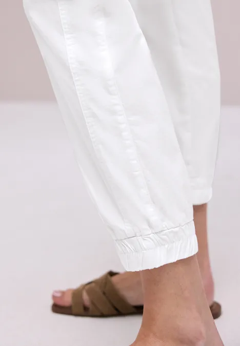 Fuß und Knöchel in weißen Jogginghosen und braunen Schlappen