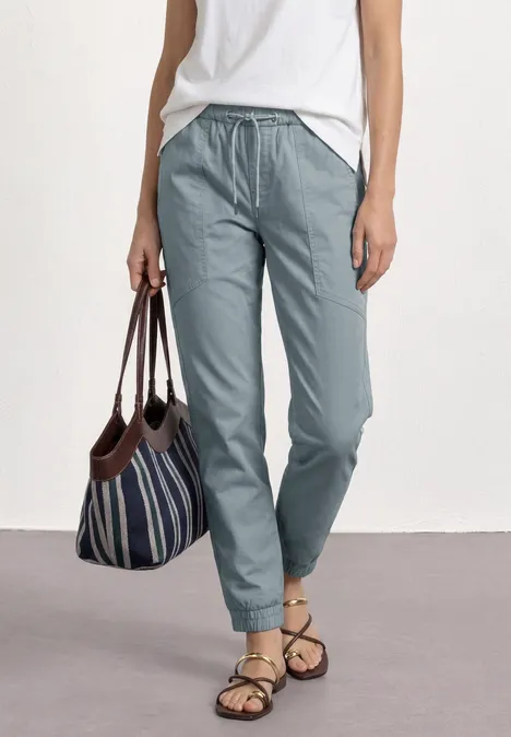 Frau trägt weiße Bluse, hellblaue Hose, gestreifte Tasche und Sandalen.