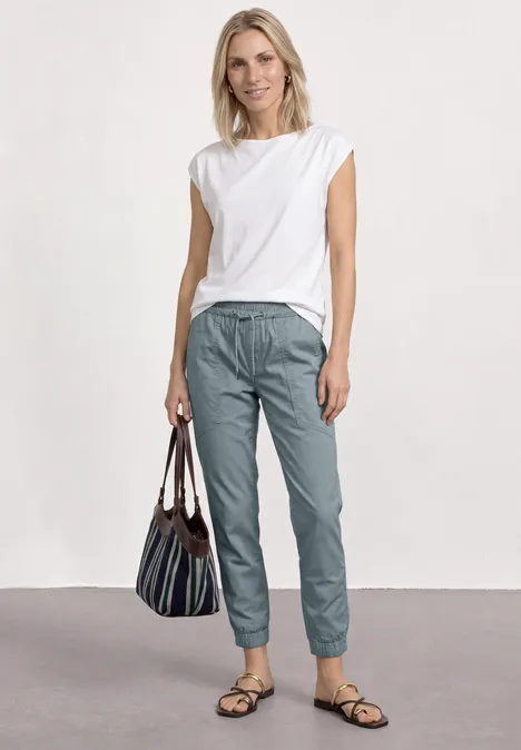 Eine Frau in weißem Top und graublauen Hose mit gestreifter Tasche.