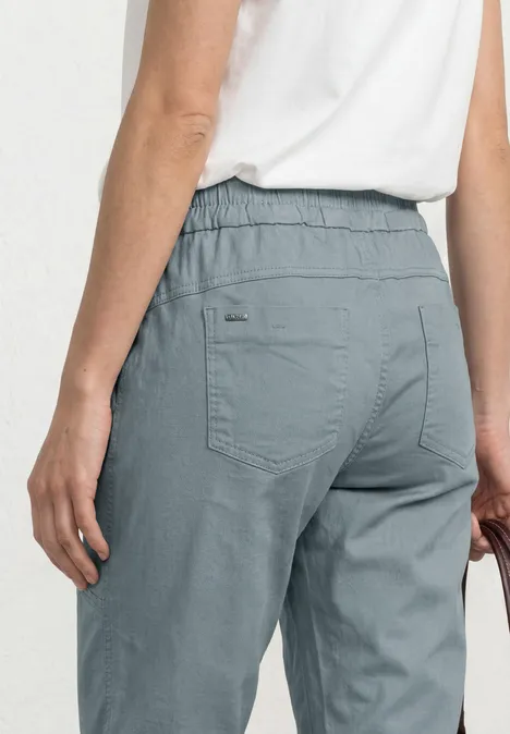 Rückansicht: Blaugraue Chino-Hose mit Gummibund und Gesäßtaschen, getragen zu weißem T-Shirt.