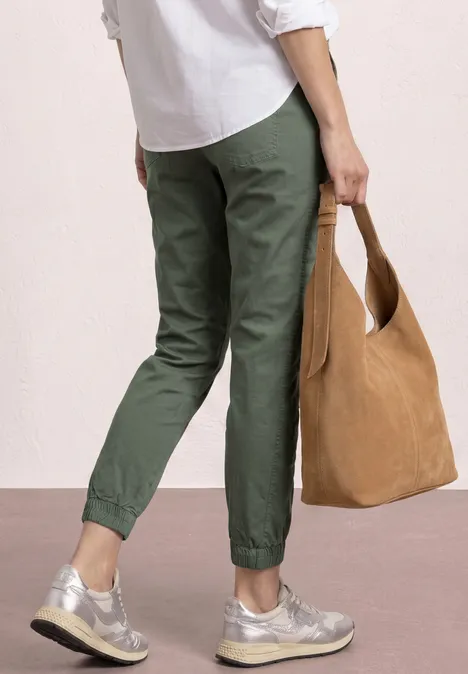 Person von hinten, trägt olivgrüne Hose, graue Sneaker und hält eine braune Tasche.