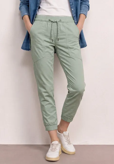 Person trägt hellgrüne Chinohose und weiße Sneakers.