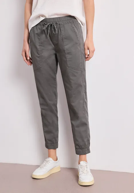 Person trägt graue, lockere Hose mit Tunnelzug und weiße Sneaker.