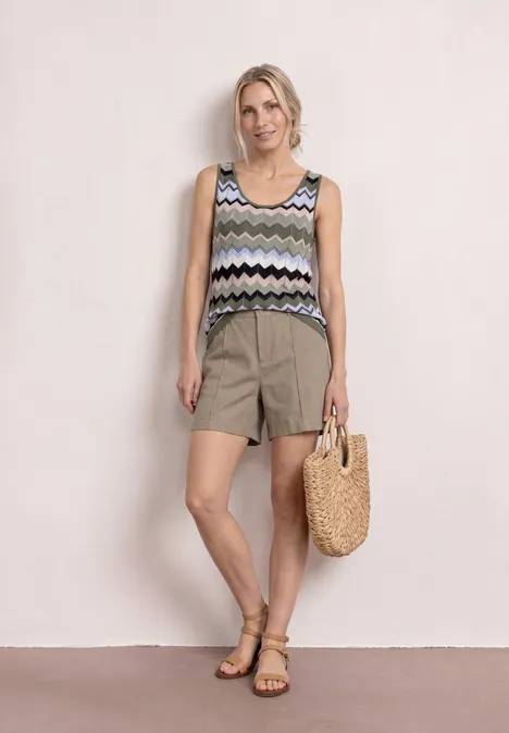 Vrouw in mouwloze, gehaakte top met motief, luchtige short, sandalen en gevlochten strooien tas.