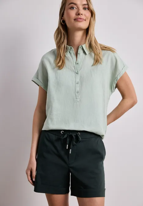 Persoon in lichtgroen overhemd met korte mouwen en zwarte shorts voor een lichte achtergrond