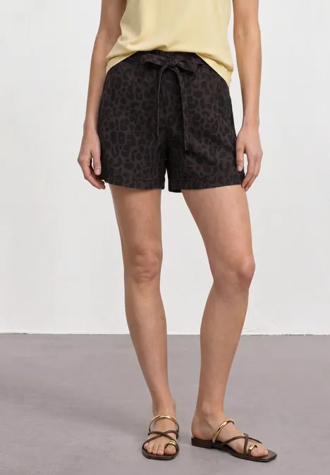 Frau trägt schwarze, gemusterte Shorts mit Tunnelzug und flache Sandalen.