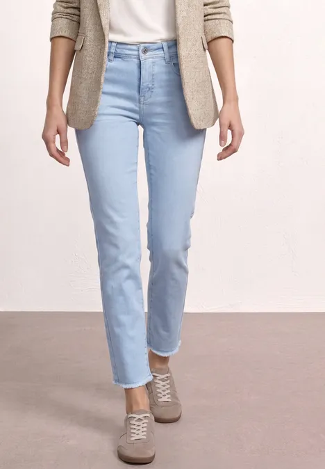 Femme portant un jean clair, un cardigan beige et des baskets confortables sur fond neutre.