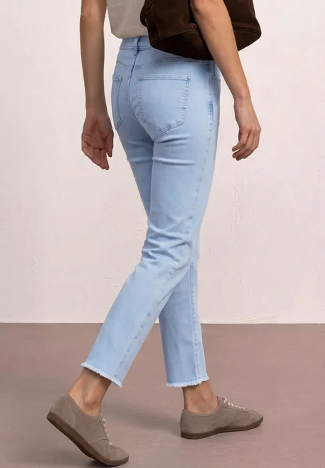 Personne porte un jean bleu clair, des slip-ons marron et un sac épaule marron sur fond clair.