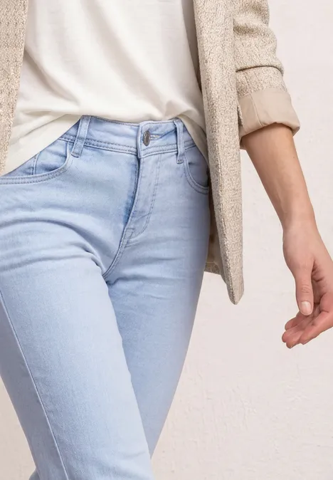 Gros plan sur un torse portant un jean bleu clair, un t-shirt blanc et un blazer beige.