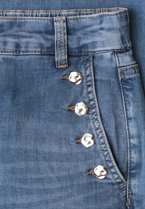 Jean bleu avec boutons décoratifs argentés alignés le long de la poche latérale