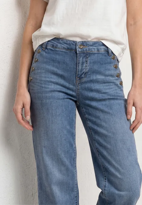 Gros plan sur une personne portant un jean taille haute bleu clair et un haut blanc devant un mur clair.