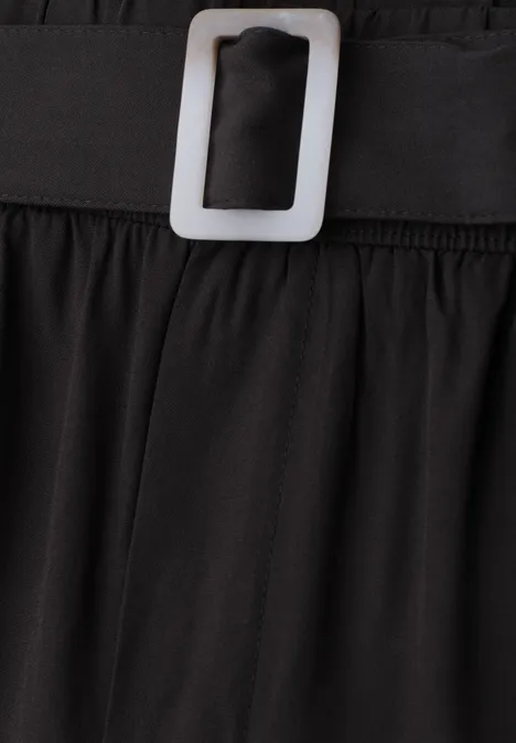 Nahaufnahme eines schwarzen Kleides mit elastischem Bund und silberner Rechteckschließe.