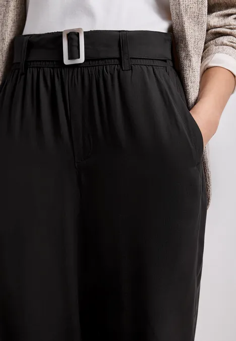 Schwarze, hochgeschnittene Hose mit Gürtel und Seitentaschen, dazu helles Oberteil und Strickjacke.