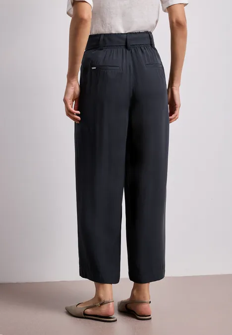 Rückansicht einer Person in weitem, knöchellangem, schwarzem Hosenmodell mit legeren Sandalen.