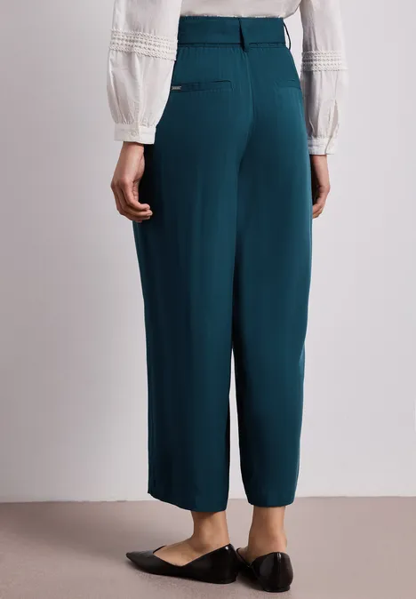 Rückansicht: Frau mit weißer Bluse, grünen weiten Anzughosen und schwarzen Slippern.