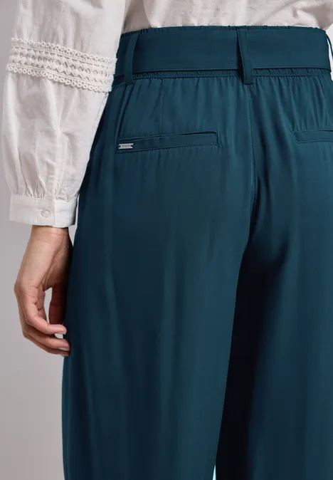 Rückansicht einer Frau in weißer Bluse mit Stickereien und tiefpetrolfarbenen Hosen mit Gummibund.