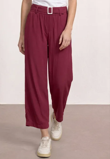 Bordeauxrode, wijde taillebroek met ceintuur en plooien, gecombineerd met witte sneakers.