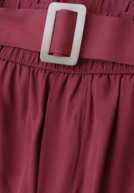Close-up van een bordeaux kledingstuk met elastische tailleband en witte gesp.