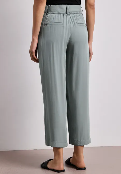 Achteraanzicht: wijde grijze broek met elastische tailleband en zijzakken, tot op de enkels.