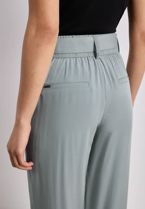 Achteraanzicht van een persoon met een los vallende grijsgroene broek met elastische taille en achterzakken.