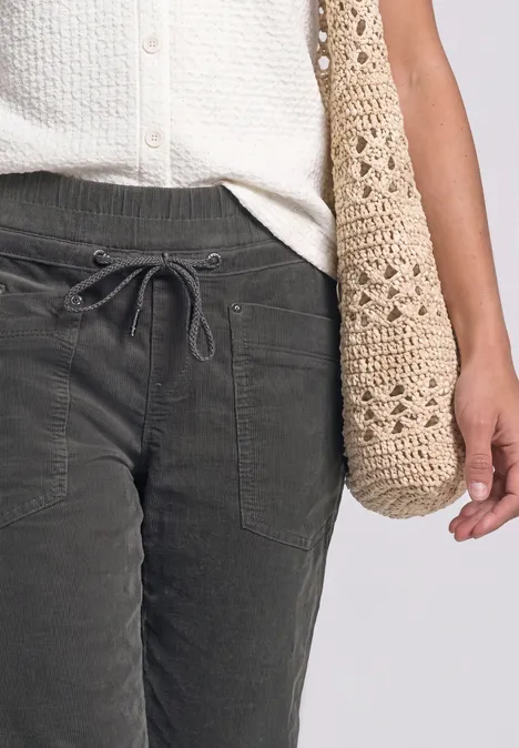 Dunkelgraue Cordhose mit Taschen und Tunnelzug, weiße Bluse, gehäkelte Schultertasche.
