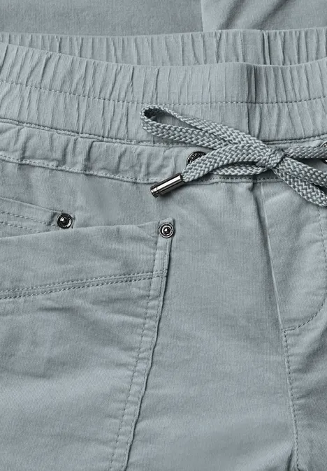 Nahaufnahme einer grauen Jogginghose mit Kordelzug, Bundfalten und Taschen mit Nieten