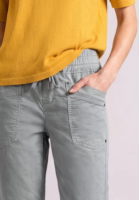 Person trägt graue Freizeithose mit Taschen und senfgelbes T-Shirt, Ausschnitt von Brust bis Hüfte.
