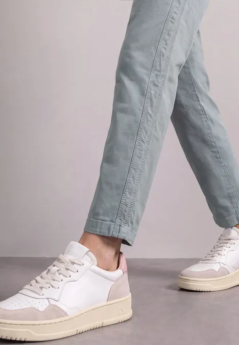 Weiße Sneaker mit beigen Sohlen, getragen zu hellgrünen, knöchellangen Hosen.