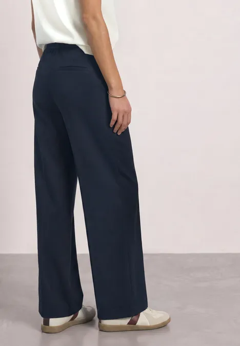 High Waist Straight Leg Hose im Casual Fit shadowed navy Frau von hinten in weißem Top und weiten, dunkelblauen Hosen sowie hellen Schuhen.