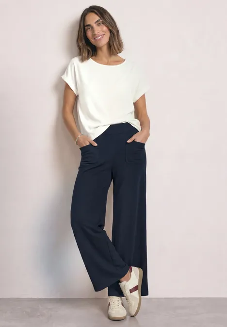 High Waist Straight Leg Hose im Casual Fit shadowed navy Frau im weißen T-Shirt und weiten schwarzen Hosen steht lächelnd mit Händen in den Taschen.