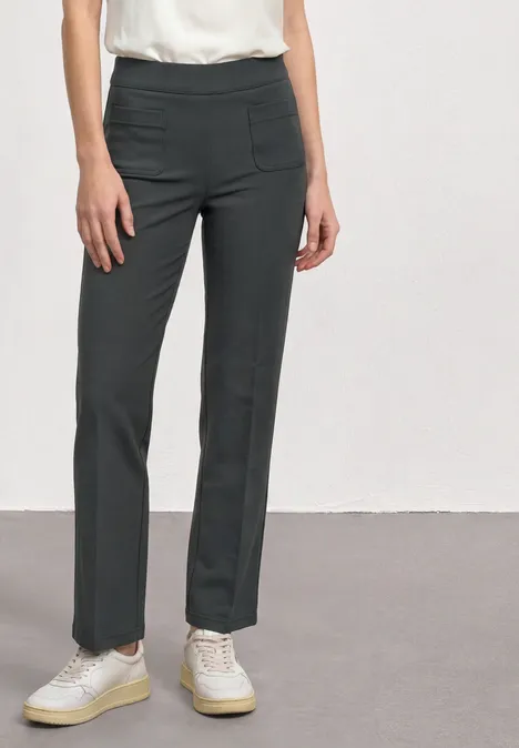 High Waist Straight Leg Hose im Casual Fit mossbound green Frau trägt gerade geschnittene, dunkle Hose mit seitlichen Taschen, weißes Top und weiße Sneaker.