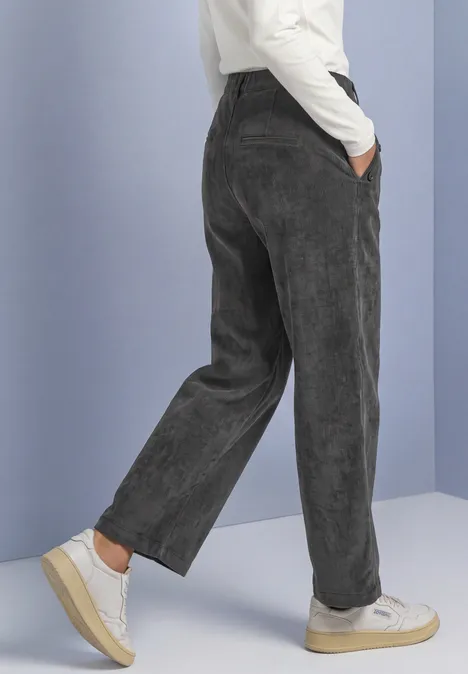 Broek met Mid Waist-taille en Straight Leg-pijpen, met knopen gravel grey Persoon in wijde, antracietgrijze corduroy broek en witte sneakers voor een pastelgekleurde achtergrond.