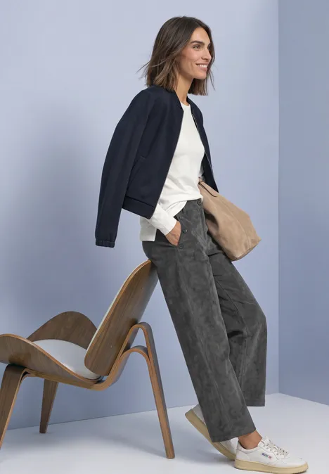 Broek met Mid Waist-taille en Straight Leg-pijpen, met knopen gravel grey Vrouw in casual look met donkere jas, wit T-shirt en wijde corduroy broek, staand bij een houten stoel.