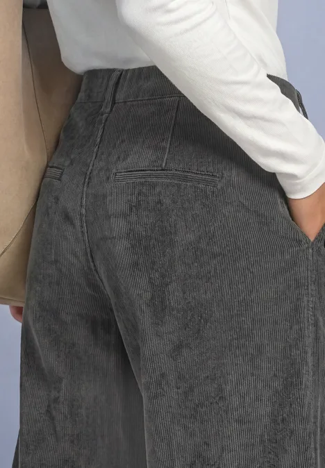 Broek met Mid Waist-taille en Straight Leg-pijpen, met knopen gravel grey Een persoon van achteren in zwarte high-waist jeans, hand in de zak, wit shirt en beige schouderband.