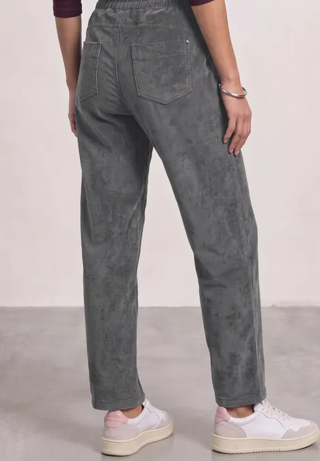 Mid Waist straight leg corduroybroek met rechte pijpen en middelhoge taille gravel grey Achteraanzicht van persoon in losse grijze broek en witte sneakers op lichte vloer.