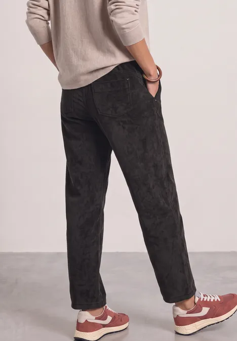 Mid Waist Straight Leg Cordhose in Unifarbe black coffee Rückansicht einer Person in schwarzen, samtigen Hosen und roten Sneakern vor hellem Hintergrund.