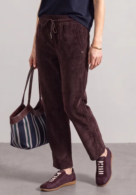 Mid Waist straight leg corduroybroek met rechte pijpen en middelhoge taille vintage ruby Persoon draagt donkerbruine corduroy broek, bordeauxrode sneakers en houdt een gestreepte tas vast.