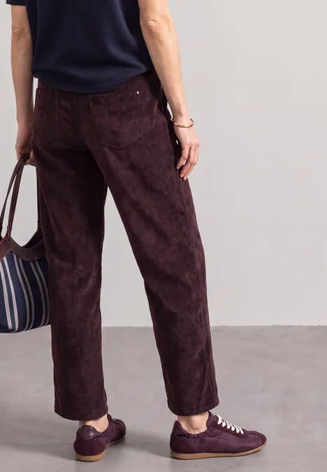 Mid Waist straight leg corduroybroek met rechte pijpen en middelhoge taille vintage ruby Rugaanzicht van een persoon met donkerbruine broek, paarse sneakers en gestreepte tas.