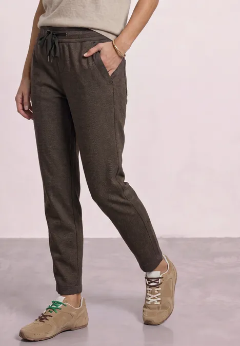 Donkerbruine linnen broek met verstelbaar koord, smalle pasvorm en zijzakken, gecombineerd met beige sneakers.