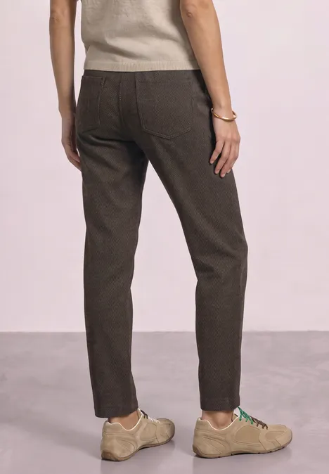 Persoon van achteren in bruine broek en beige schoenen voor een neutrale achtergrond.