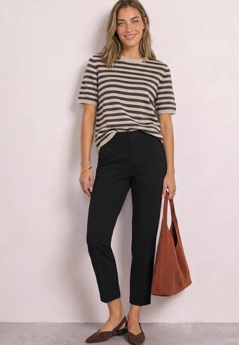 Femme en t-shirt à rayures, pantalon noir et sac marron sur fond clair