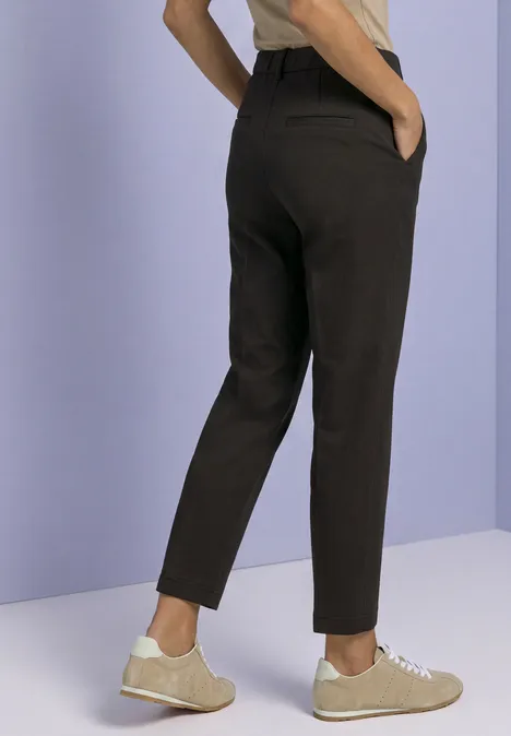 Pantalon gris foncé coupe slim avec poches latérales, porté avec des baskets claires.