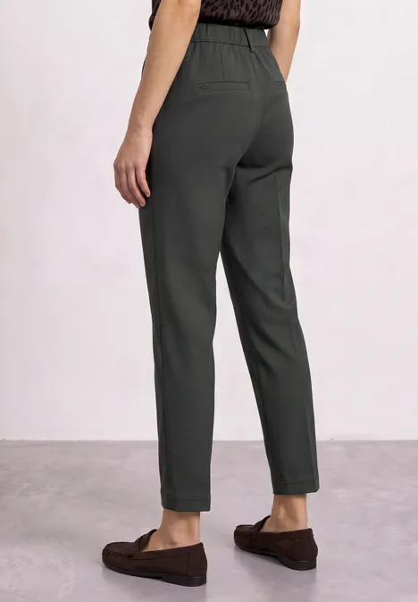 Spodnie chino Slim Leg z brokatowymi akcentami mossbound green Widok od tyłu: osoba w ciemnozielonych, wąskich spodniach i brązowych mokasynach.