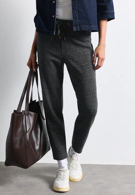Personne portant un pantalon gris ample, baskets blanches et un grand sac en cuir marron.