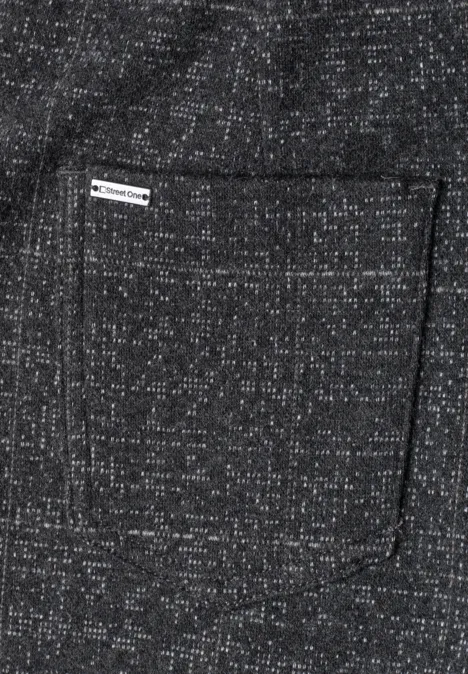 Une poche carrée cousue sur un tissu gris chiné à petits motifs blancs, ornée d’une étiquette tissée.