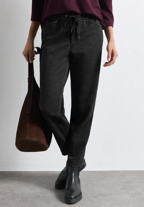 Femme porte un pantalon noir décontracté avec cordon, bottines noires et un sac marron.