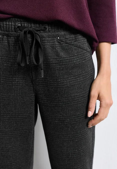 Main de profil à côté d'une personne en pantalon de jogging à carreaux gris foncé avec cordon et haut bordeaux.