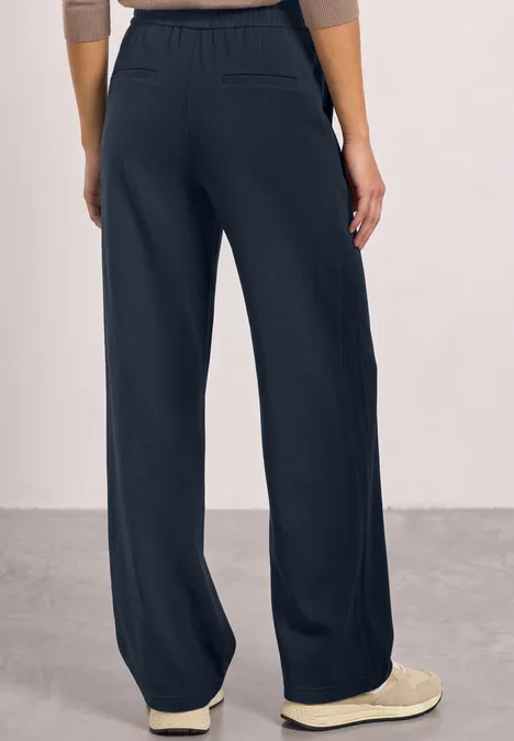 Frau trägt weite dunkelblaue Hose mit hohem elastischem Bund und helle Slipper.