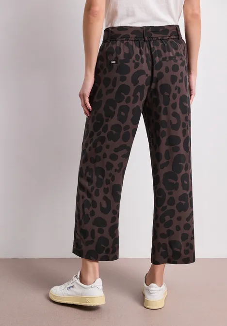 Vue de dos : personne en baskets blanches, pantalon large imprimé léopard marron et T-shirt blanc.